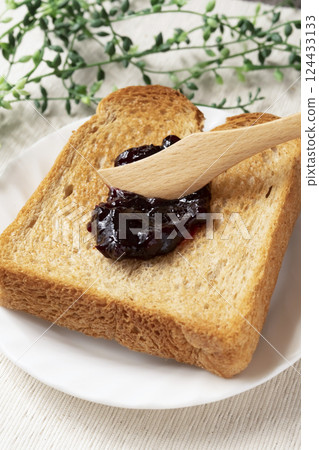 Spread bottled blueberry jam onto toasted bread Spread bottled blueberry jam onto toasted bread 124433133