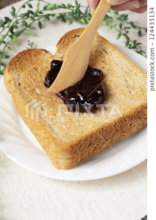 Spread bottled blueberry jam onto toasted bread Spread bottled blueberry jam onto toasted bread 124433134