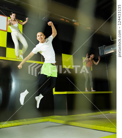 Cheerful young man jumping in modern indoor trampoline park 124433135