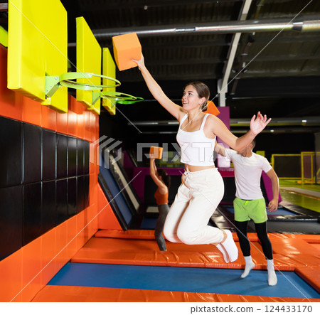 Cheerful girl throwing foam cube into basketball hoop in trampoline park Cheerful girl throwing foam cube into basketball hoop in trampoline park 124433170