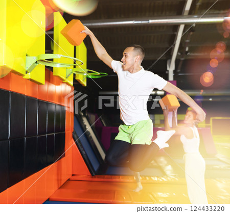 Cheerful man playing basketball with foam cube at trampoline park 124433220