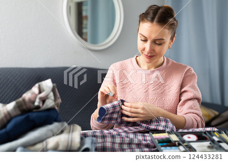 Woman repairing clothes with a needle and thread Woman repairing clothes with a needle and thread 124433281