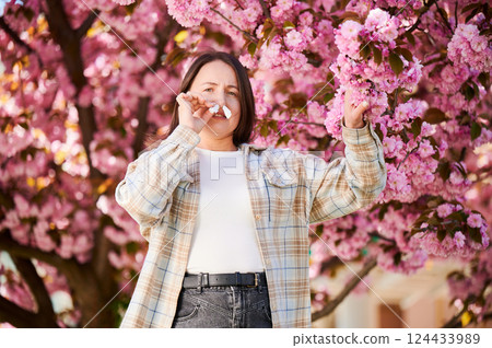Woman allergic suffering from seasonal allergy and runny nose disease at spring. Young woman with paper tissues inserted into nose - symbolic gesture of inability to breathe due to nasal congestion. Woman allergic suffering from seasonal allergy and runny nose disease at spring. Young woman with paper tissues inserted into nose - symbolic gesture of inability to breathe due to nasal congestion. 124433989