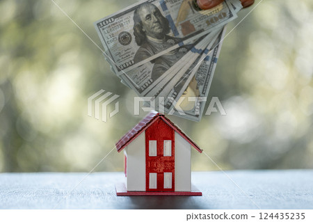Model of house with dollar bill on table on blurred background. Money saving or investing for home loan or real estate. Investment property, Saving money for retirement concept. 124435235