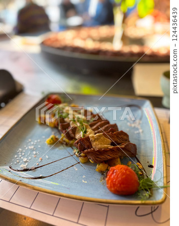 Gourmet beef steak with sauce and vegetables on ceramic plate in restaurant setting. Modern cuisine, flavor, and elegant food presentation. 124436439