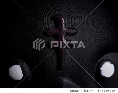 Close-Up Artistic Dark Abstract Textured Sculpture with White Eyes and Central Raised Symbol 124436956