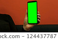 Young woman at work in office holding green mockup smartphone in hand. Woman using mobile phone with chroma key. Vertical mode. Touching, swiping display, pressing, surfing social media. Close-up 124437787