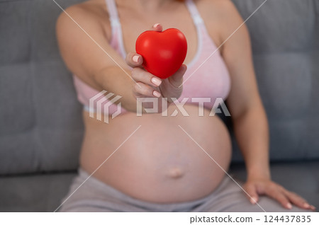 Caucasian pregnant woman holding heart on belly background. Third trimester.  124437835