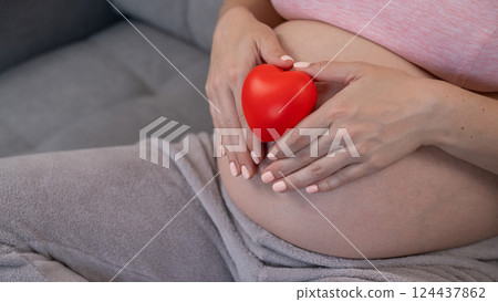 Caucasian pregnant woman holding heart on belly background. Third trimester. Caucasian pregnant woman holding heart on belly background. Third trimester. 124437862