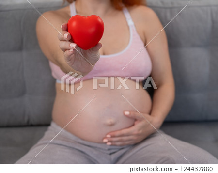 Caucasian pregnant woman holding heart on belly background. Third trimester.  124437880