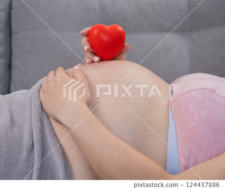 Caucasian pregnant woman holding heart on belly background. Third trimester. Caucasian pregnant woman holding heart on belly background. Third trimester. 124437886