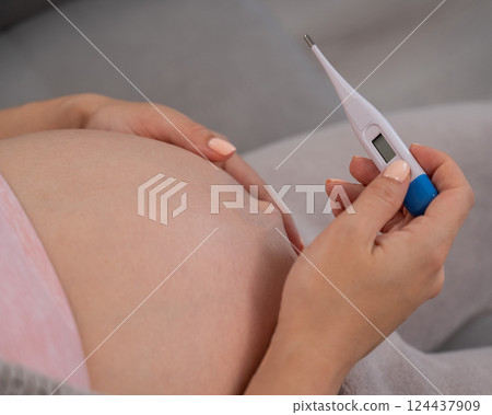Pregnant woman measures temperature. Close up of the belly. Pregnant woman measures temperature. Close up of the belly. 124437909