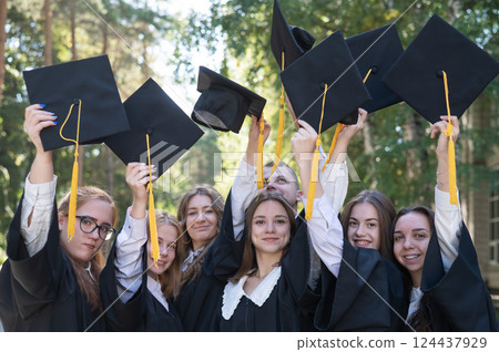 Classmates in graduation gowns throwing hats outdoors. Classmates in graduation gowns throwing hats outdoors. 124437929