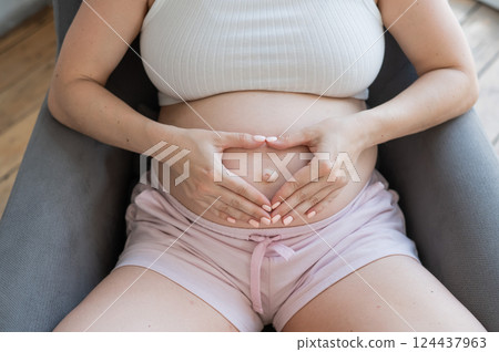 Pregnant woman holds her hands in a heart shape on her belly.  124437963