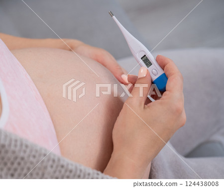 Pregnant woman measures temperature. Close up of the belly. 124438008