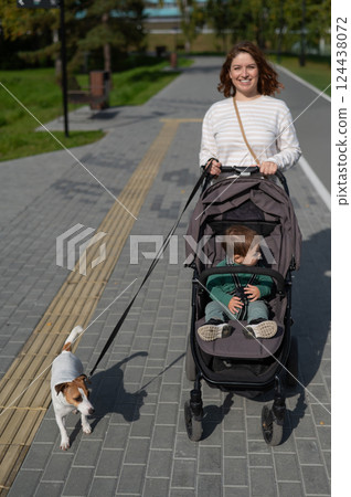 Caucasian woman walks in the park with her one-year-old son and Jack Russell Terrier dog.  124438072