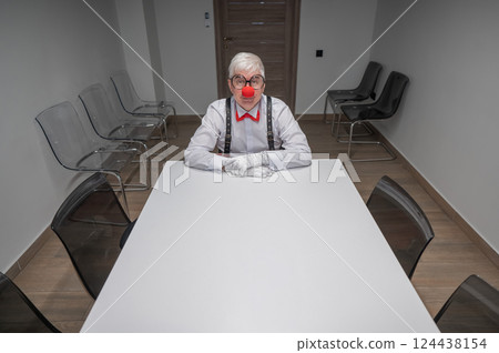 An elderly man in a clown costume sits at a desk in an office.  124438154