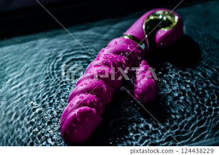 Pink ribbed vibrator in water. Circles on water around sex toy.  124438229