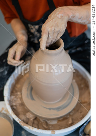 Close-up of a potter's hands making a ceramic vase on a potter's wheel. Vertical photo.  124438234