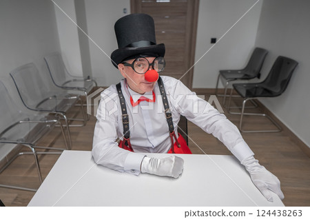 An elderly man in a clown costume sits at a desk in an office. An elderly man in a clown costume sits at a desk in an office. 124438263