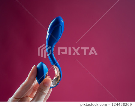 Lube pouring onto blue sex toy on pink background.  124438269
