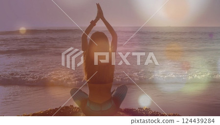 Image of light spots over caucasian woman practicing yoga at beach 124439284