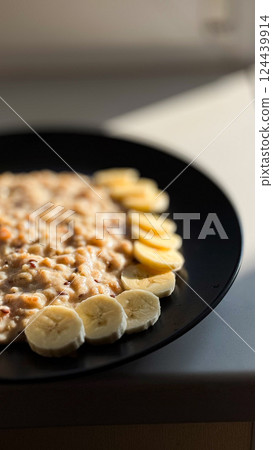 Healthy oatmeal with banana slices on a black plate in natural sunlight 124439914