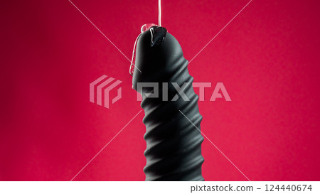 Lube pouring on black dildo on pink background.  124440674