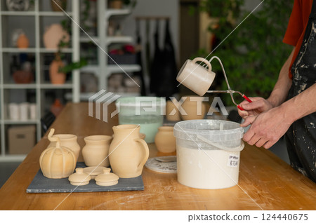 Close-up of a potter's hands glazing a ceramic mug.  124440675