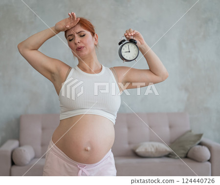 Unhappy pregnant woman holds alarm clock in anticipation of giving birth. Unhappy pregnant woman holds alarm clock in anticipation of giving birth. 124440726