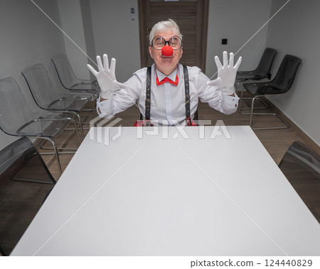 An elderly man in a clown costume sits at a desk in an office. An elderly man in a clown costume sits at a desk in an office. 124440829