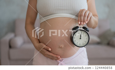 Close up of pregnant woman's belly holding alarm clock. Close up of pregnant woman's belly holding alarm clock. 124440858