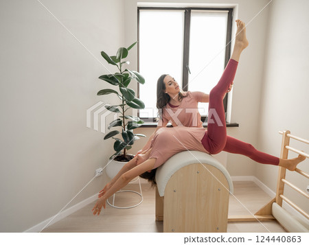 A trainer adjusts woman on a Ladder Barrel. Personal training.  124440863