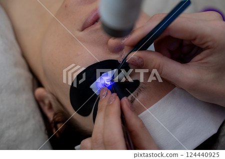 A woman undergoing eyelash extension procedure using an ultraviolet lamp. A woman undergoing eyelash extension procedure using an ultraviolet lamp. 124440925