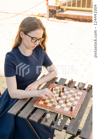 Caucasian woman playing chess outdoors. 124441004