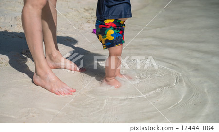 Close-up of woman's legs and her one-year-old child on the seashore.  124441084
