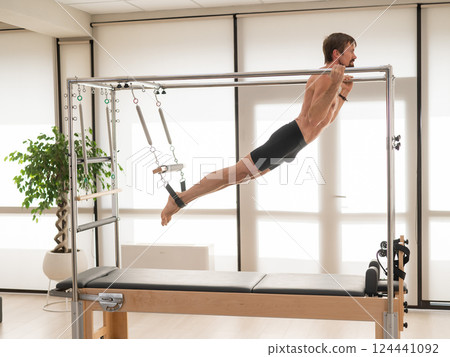 A man performs aerial exercises on a reformer machine. 124441092