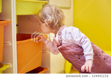 girl looks into a box with toys in a bright yellow room at home girl looks into a box with toys in a bright yellow room at home 124441218