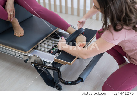 Personal Pilates training. Instructor adjusts woman on reformer. Personal Pilates training. Instructor adjusts woman on reformer. 124441276