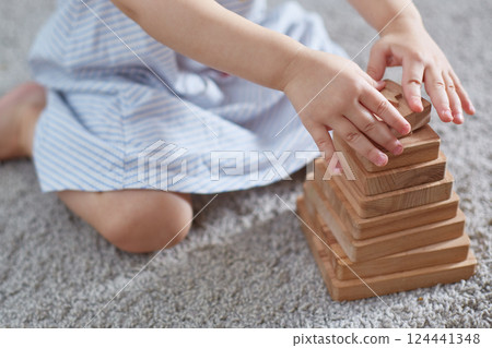 outface child is playing a wooden pyramid while sitting on a carpet. 124441348