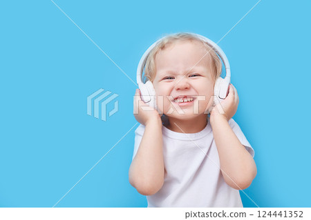 child wearing headphones and a white T-shirt listens to music on a blue background with a place for text. 124441352