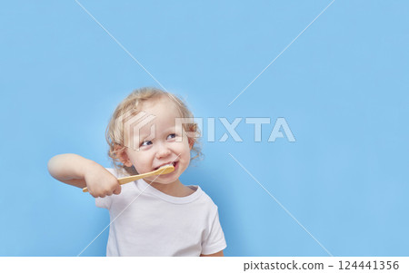 Child brushes his teeth with a wooden bamboo toothbrush on a blue background with a copy space. 124441356
