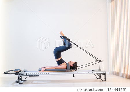 Asian woman doing pilates on reformer.  124441361