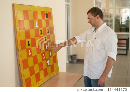 Caucasian man standing at wall mounted magnetic chessboard demonstration.  124441370