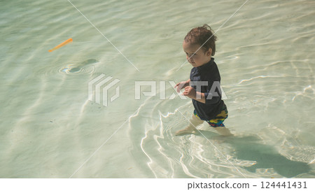 A one-year-old Caucasian boy swims in a pool with a sandy bottom.  124441431