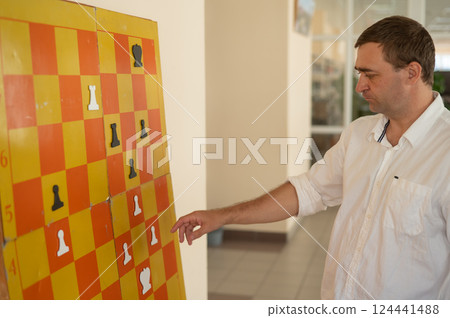 Caucasian man standing at wall mounted magnetic chessboard demonstration. Caucasian man standing at wall mounted magnetic chessboard demonstration. 124441488