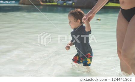 A one-year-old Caucasian boy walks hand in hand with his mother in a swimming pool. A one-year-old Caucasian boy walks hand in hand with his mother in a swimming pool. 124441502