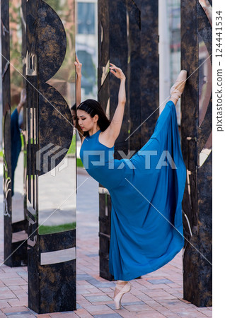 Beautiful asian ballerina in blue dress and pointe shoes posing outdoors. Vertical photo. Beautiful asian ballerina in blue dress and pointe shoes posing outdoors. Vertical photo. 124441534
