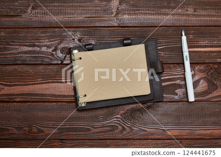 notebook with craft paper in an unfolded form lies on a wooden surface with a white fountain pen. notebook with craft paper in an unfolded form lies on a wooden surface with a white fountain pen. 124441675