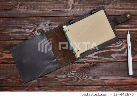 notebook with craft paper in an unfolded form lies on a wooden surface with a white fountain pen. notebook with craft paper in an unfolded form lies on a wooden surface with a white fountain pen. 124441676